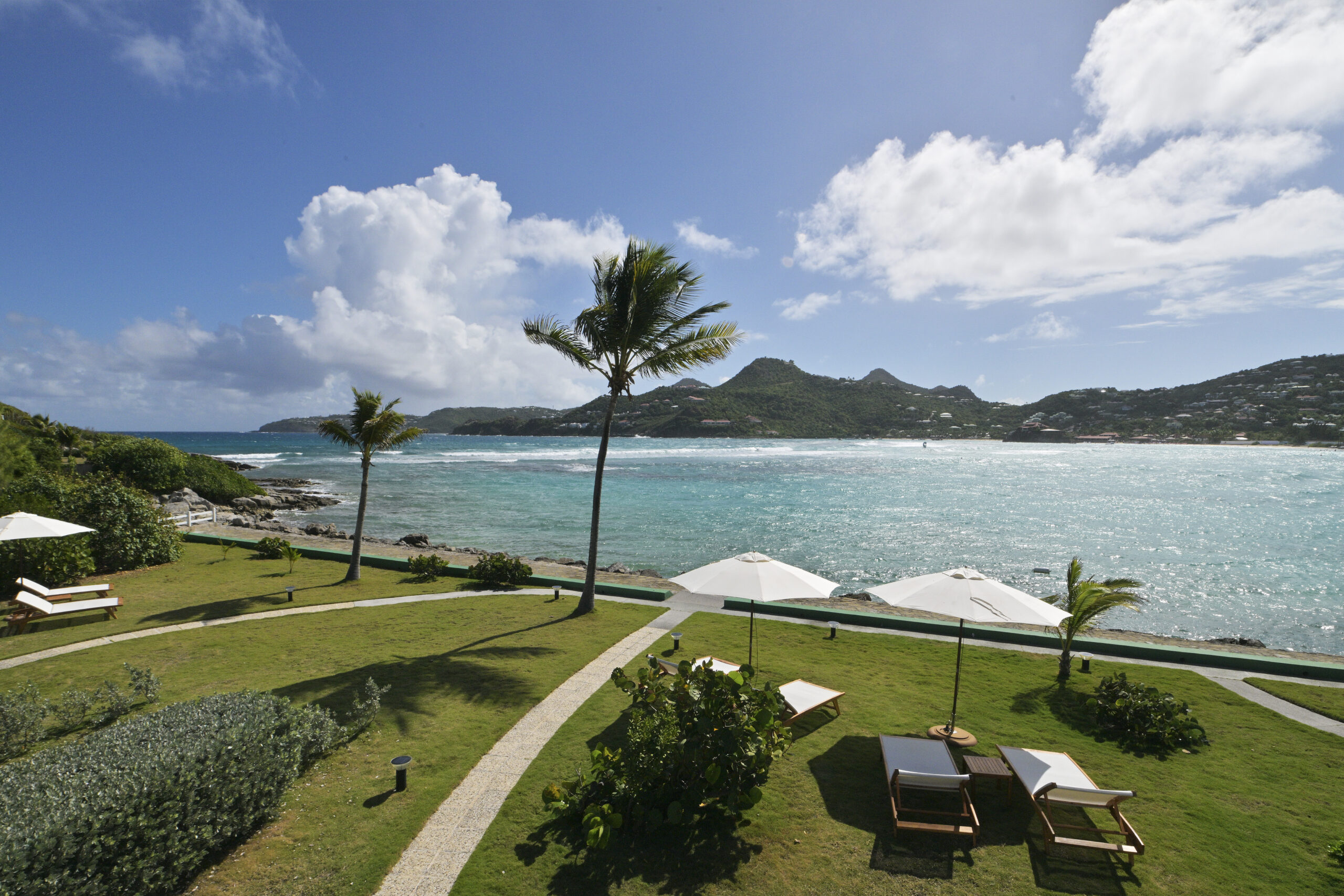 Expansive beachfront lawn with sun loungers and swaying palms overlooking turquoise waters at a St Barts luxury villa.