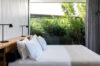 Bedroom with large windows overlooking a garden and palm trees.