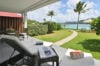 Shaded terrace with sun loungers overlooking a lush garden and turquoise bay at a beachfront St Barts villa rental.