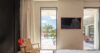 Bedroom of a St Barts villa with wicker chair, artwork, and terrace doors opening to pool and palm view.