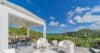 Sunlit terrace with lounge chairs and dining area overlooking the Caribbean Sea and lush hills in a St Barts villa rental.