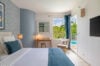 Bright villa bedroom with blue accents, writing desk, and poolside garden views in St Barts