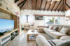 Bright villa living room with vaulted wooden ceiling, stone accent wall, sectional sofa, and ocean view in St Barts rental