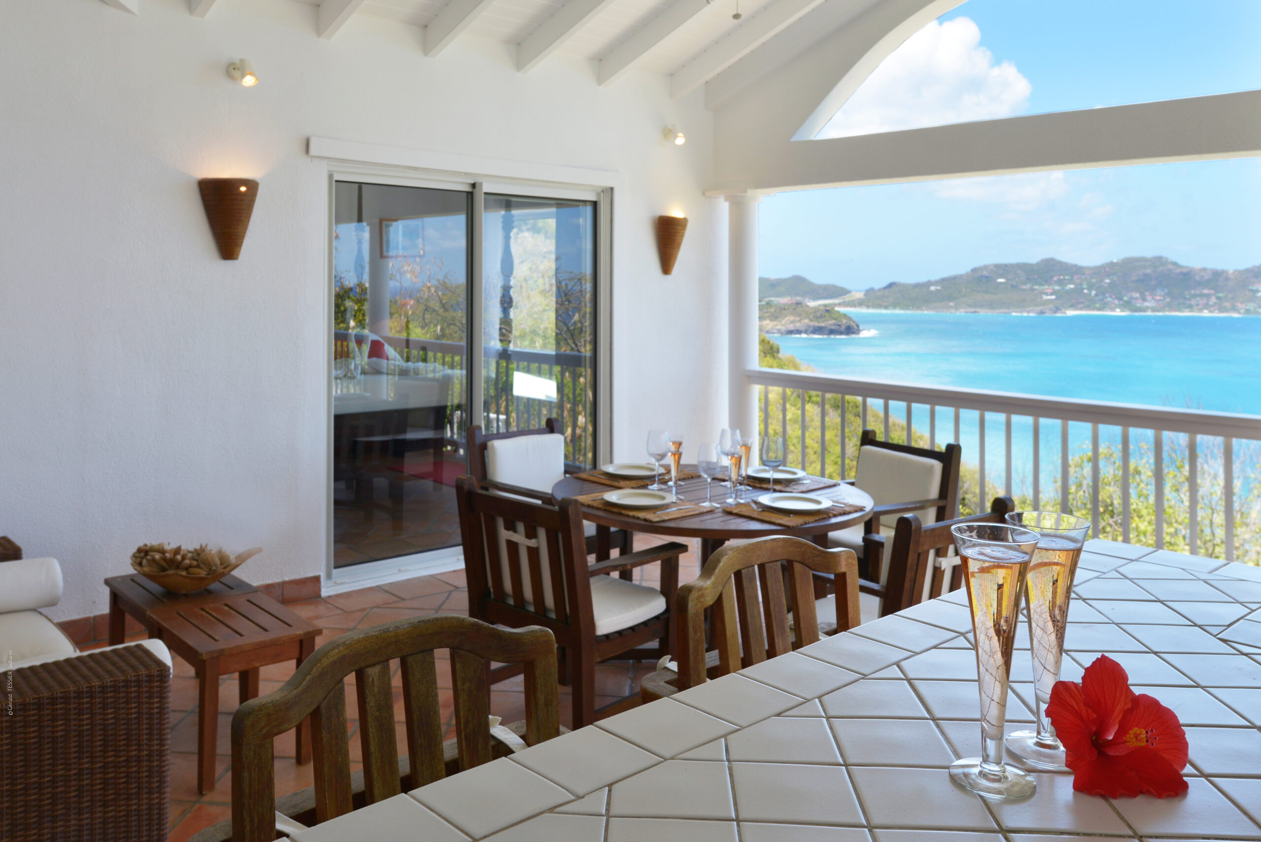 Seaside terrace at a St Barts villa with set dining table, champagne glasses, and turquoise bay views.