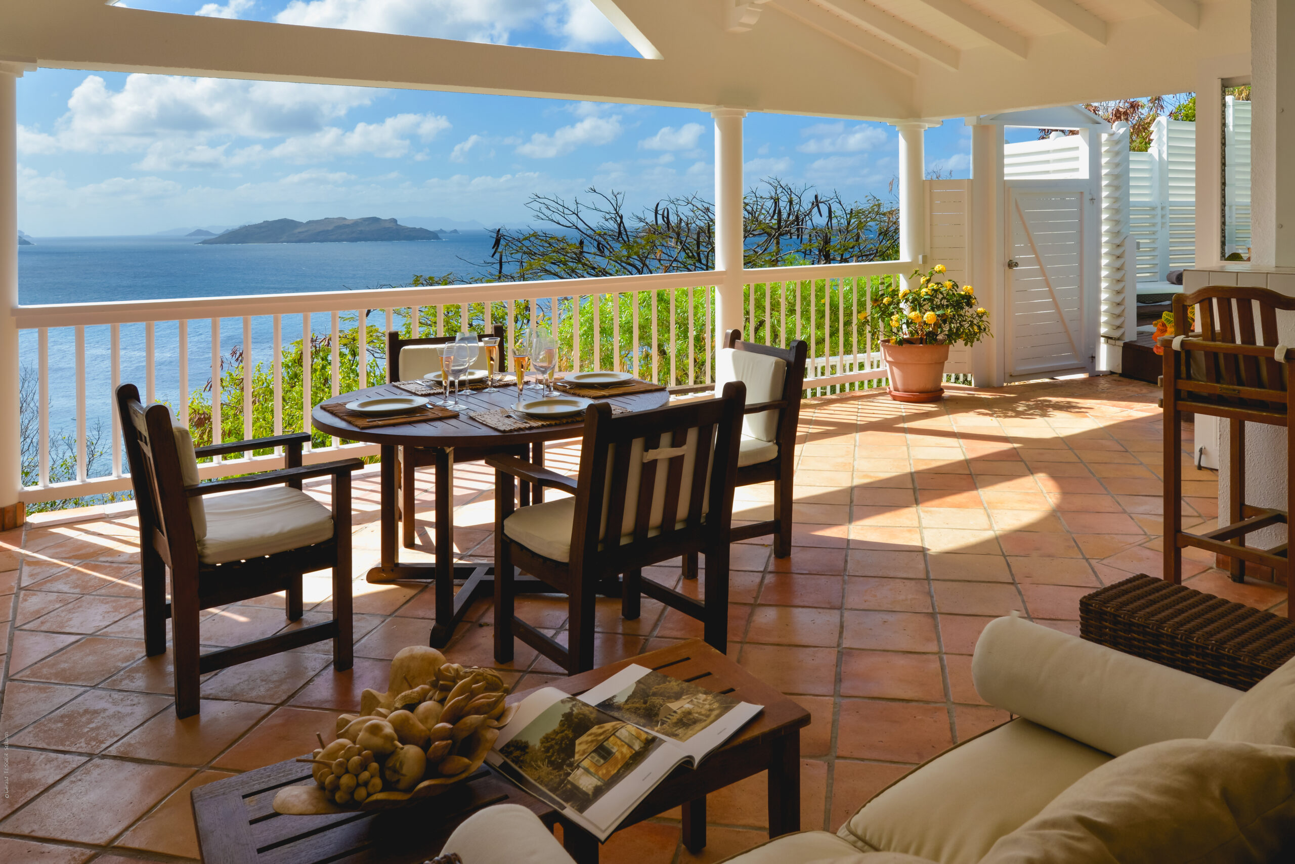 Covered terrace at a St Barts villa with ocean views, terracotta floors, and a set dining table.