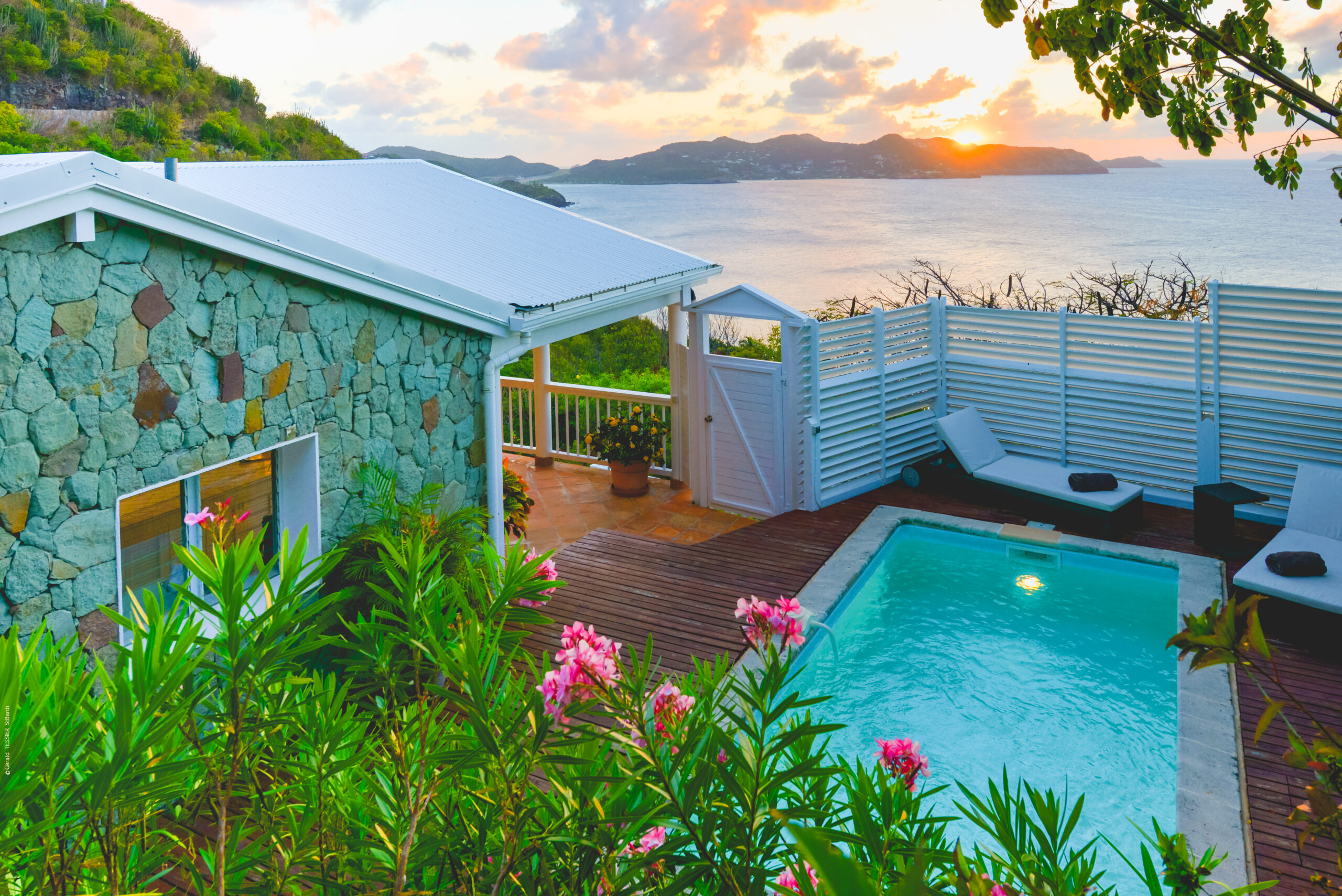 Private pool at a stone-clad St Barts villa with sun loungers and sunset ocean views.