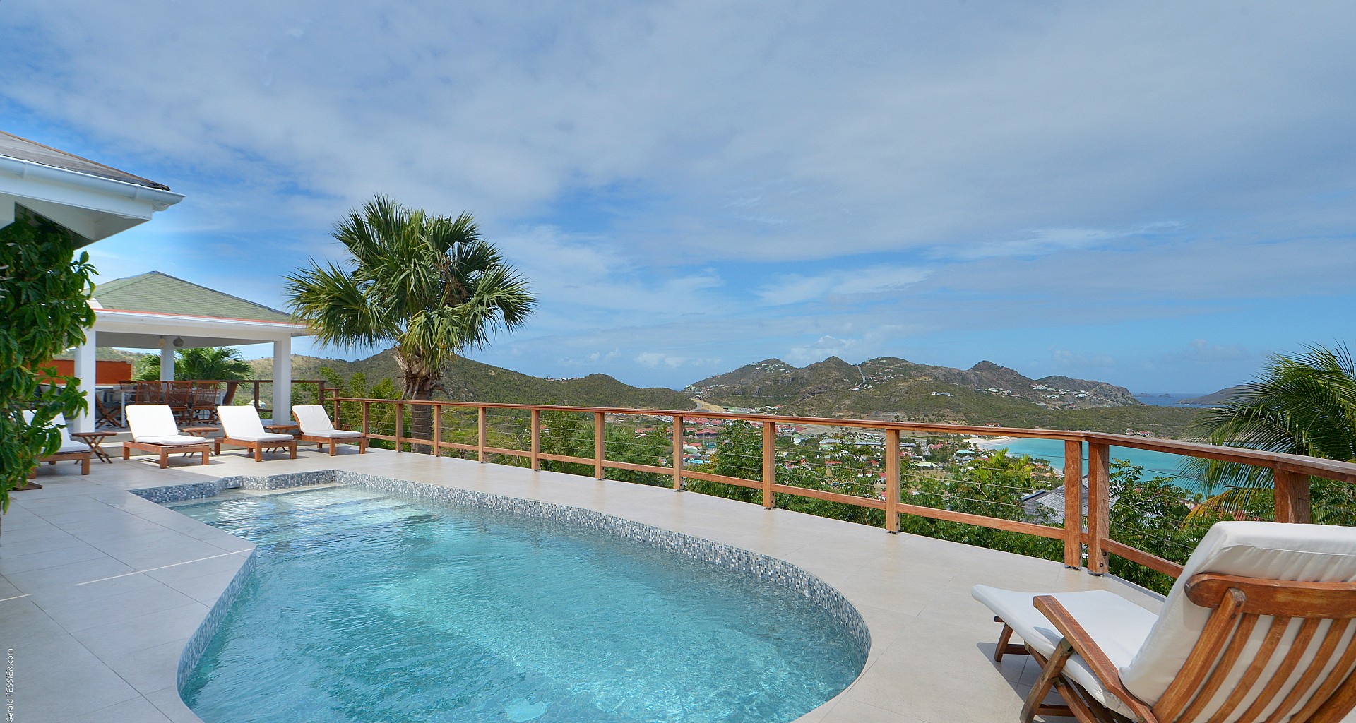 Curved swimming pool with wooden deck chairs and panoramic ocean views at a hillside St Barts villa rental.