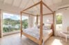 Sunlit villa bedroom with wooden four-poster bed and panoramic hillside views in a St Barts luxury rental.