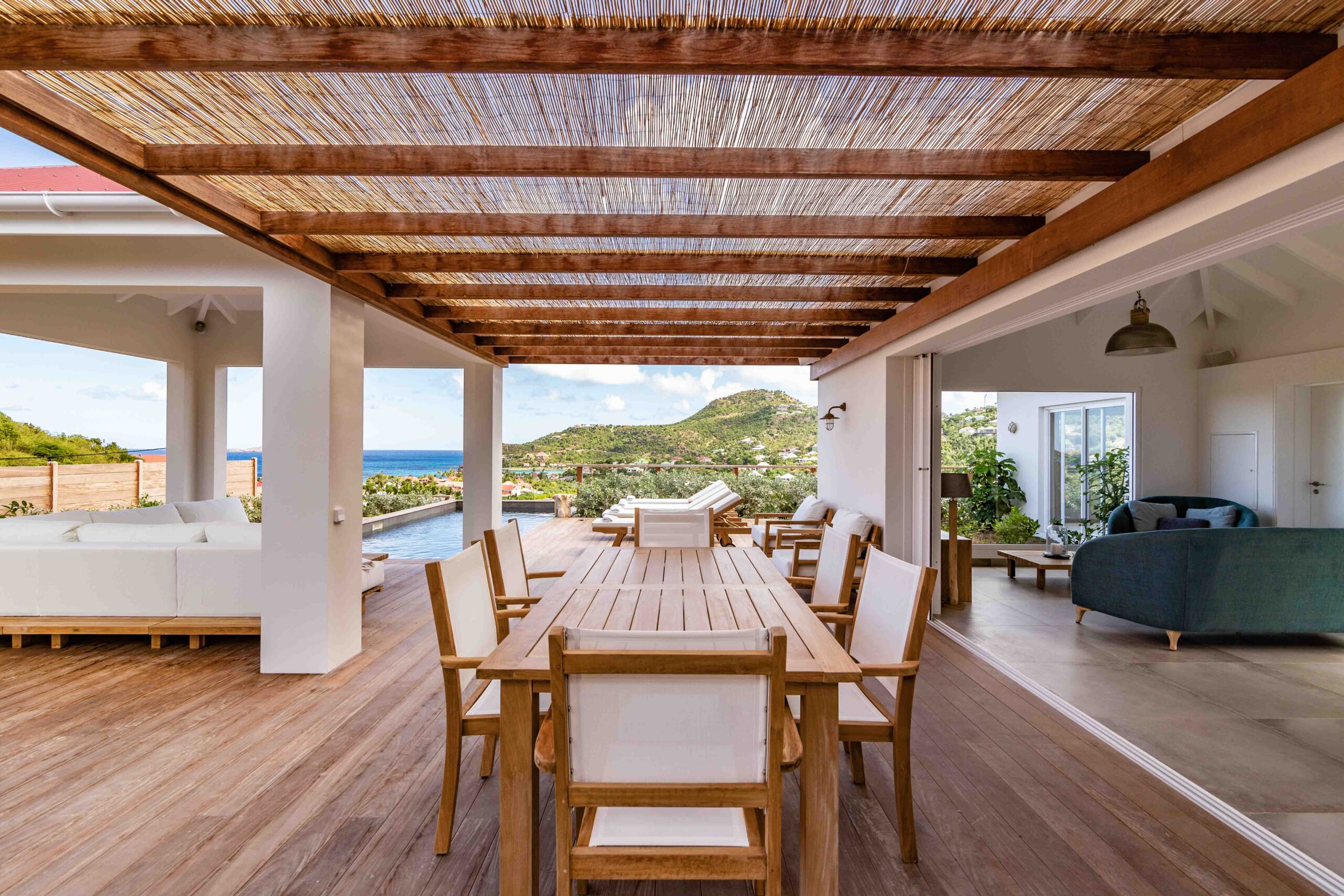 Shaded outdoor dining area with wooden table and hillside views connecting to open living spaces in a St Barts villa rental.
