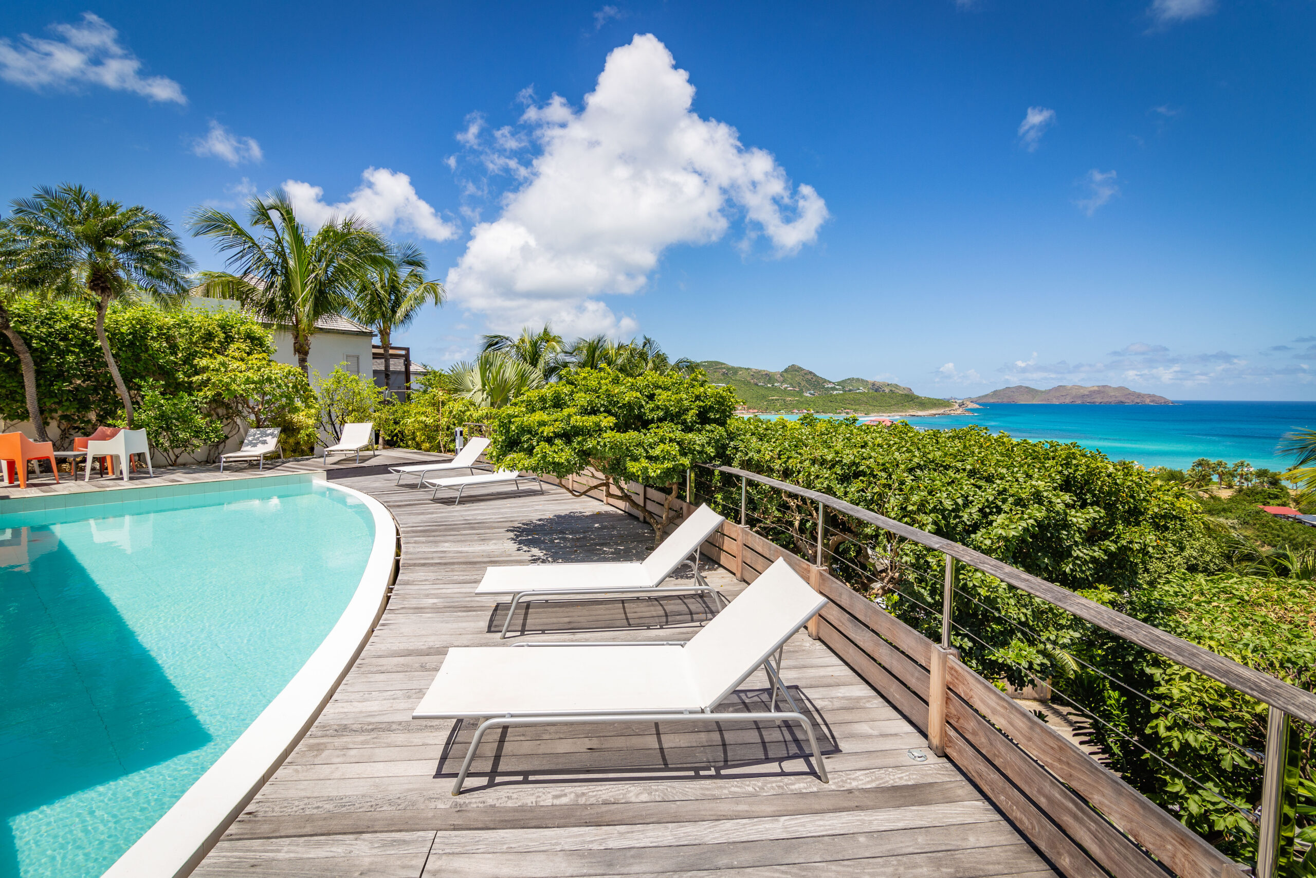 Sun loungers by a curved pool at a St Barts vacation rental with sweeping Caribbean sea views.