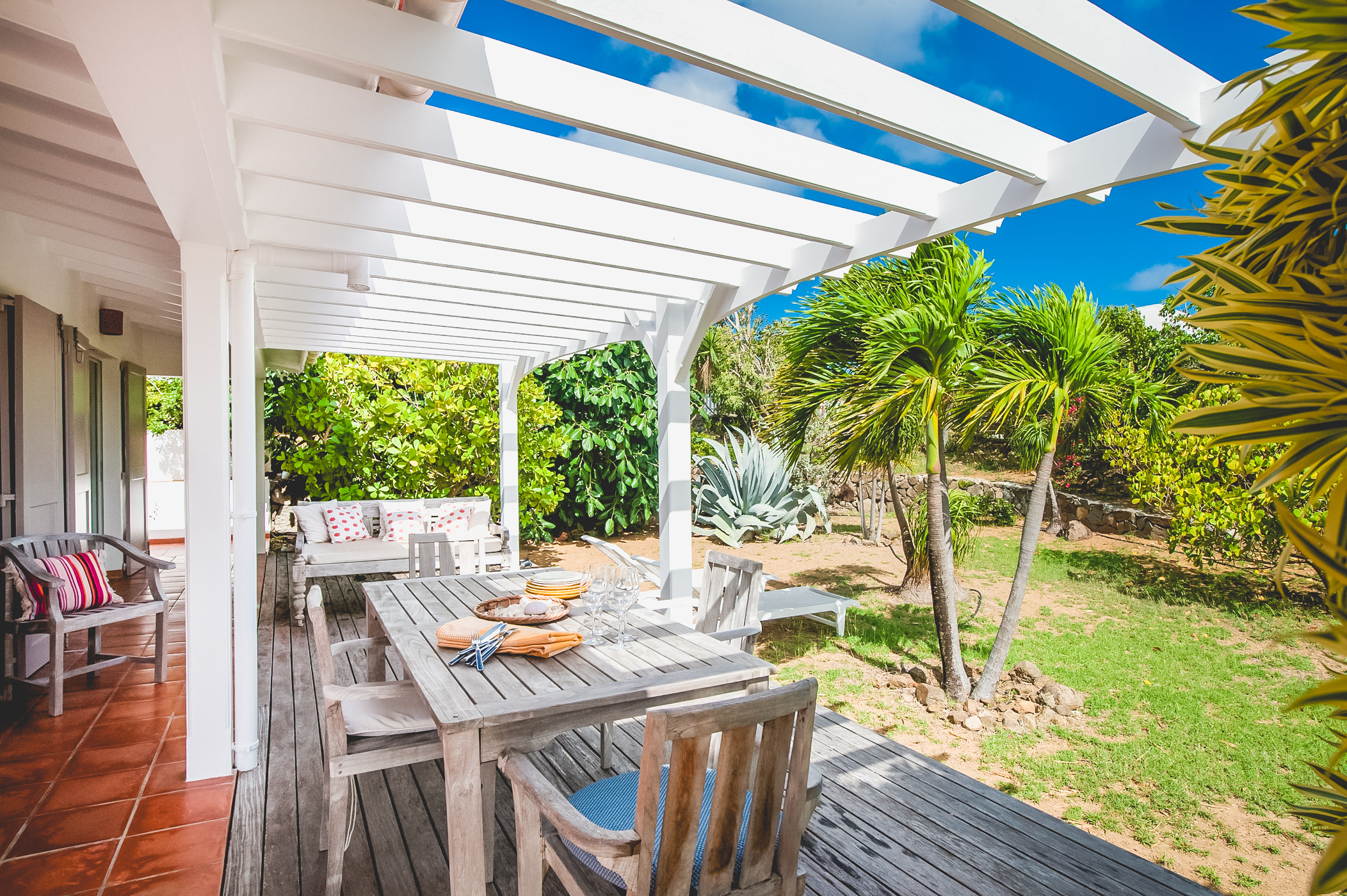 Villa terrace with white pergola, wooden dining table, and garden views in St Barts private villa rental.