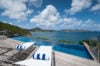 Infinity pool with wooden deck and sun loungers overlooking the Caribbean Sea and rolling green hills in St Barts.