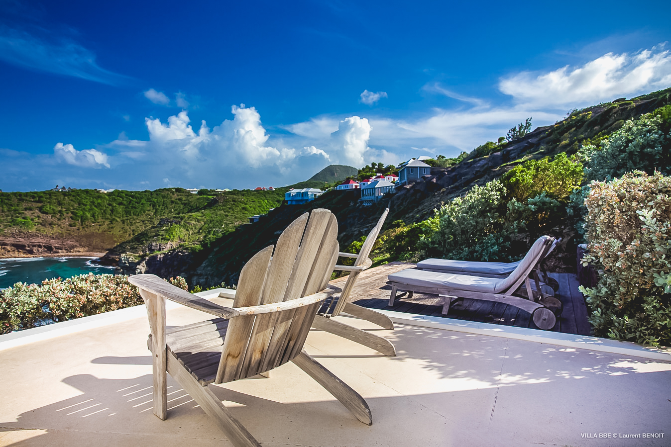 Sunny terrace with wooden lounge chairs overlooking lush hills and the Caribbean Sea in St Barts villa rental