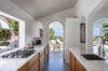 Contemporary kitchen in a St Barts villa with sleek countertops, gas range, and open archway leading to a sunlit terrace.