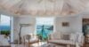 Elegant villa living room with white sofas, coastal décor, and panoramic ocean view framed by wide glass doors in St Barts.