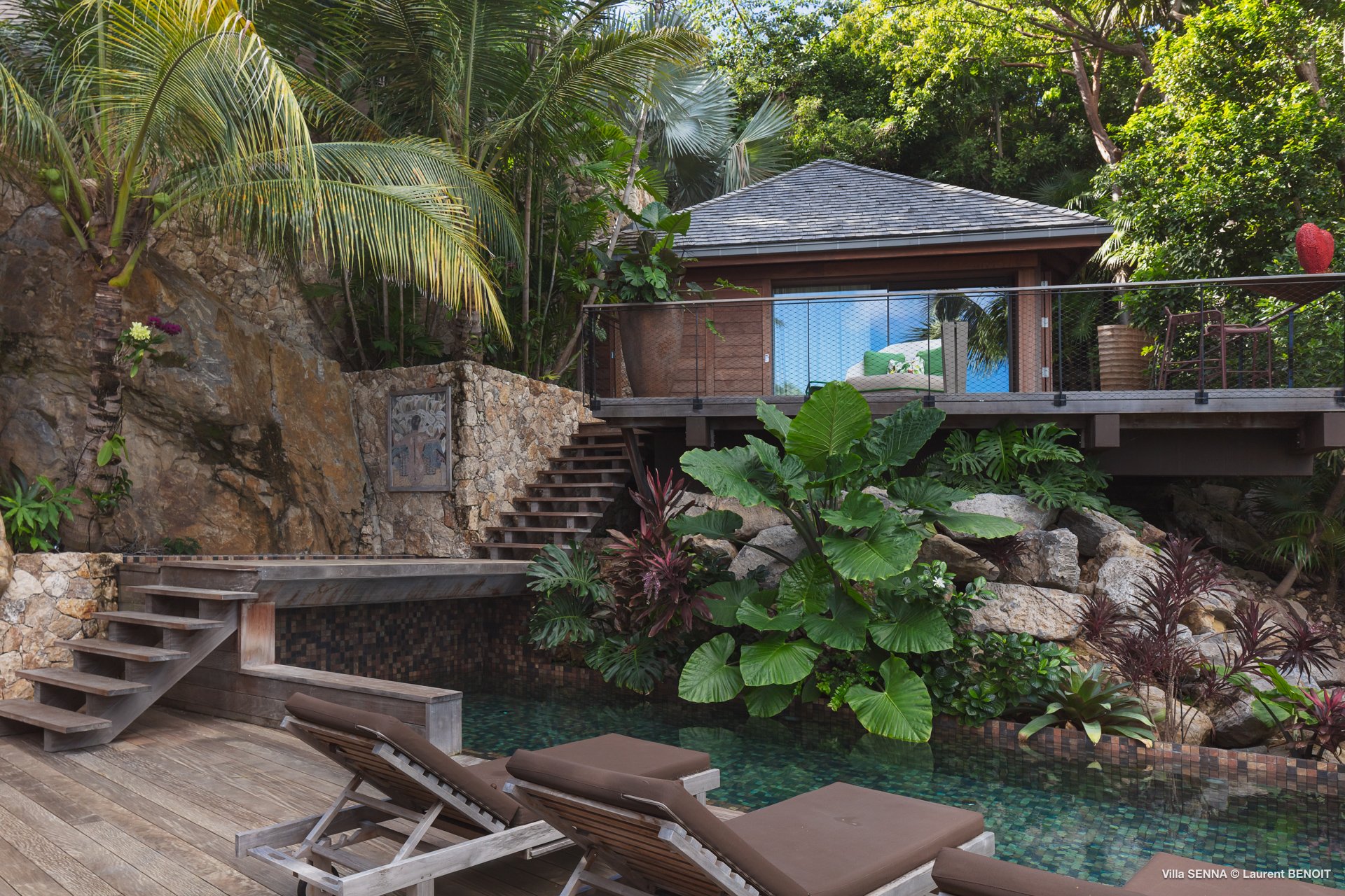 Secluded villa pool in St Barts surrounded by stone walls, lush tropical plants, and a hillside bungalow with private terrace.