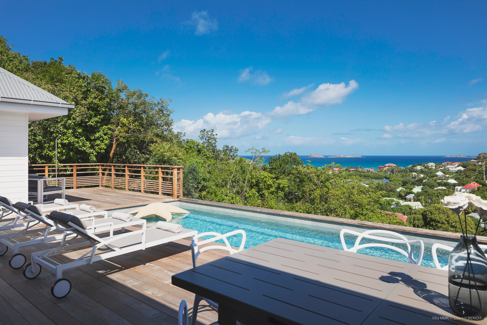 Poolside terrace with sun loungers and outdoor dining table overlooking the Caribbean Sea at a St Barts villa rental.