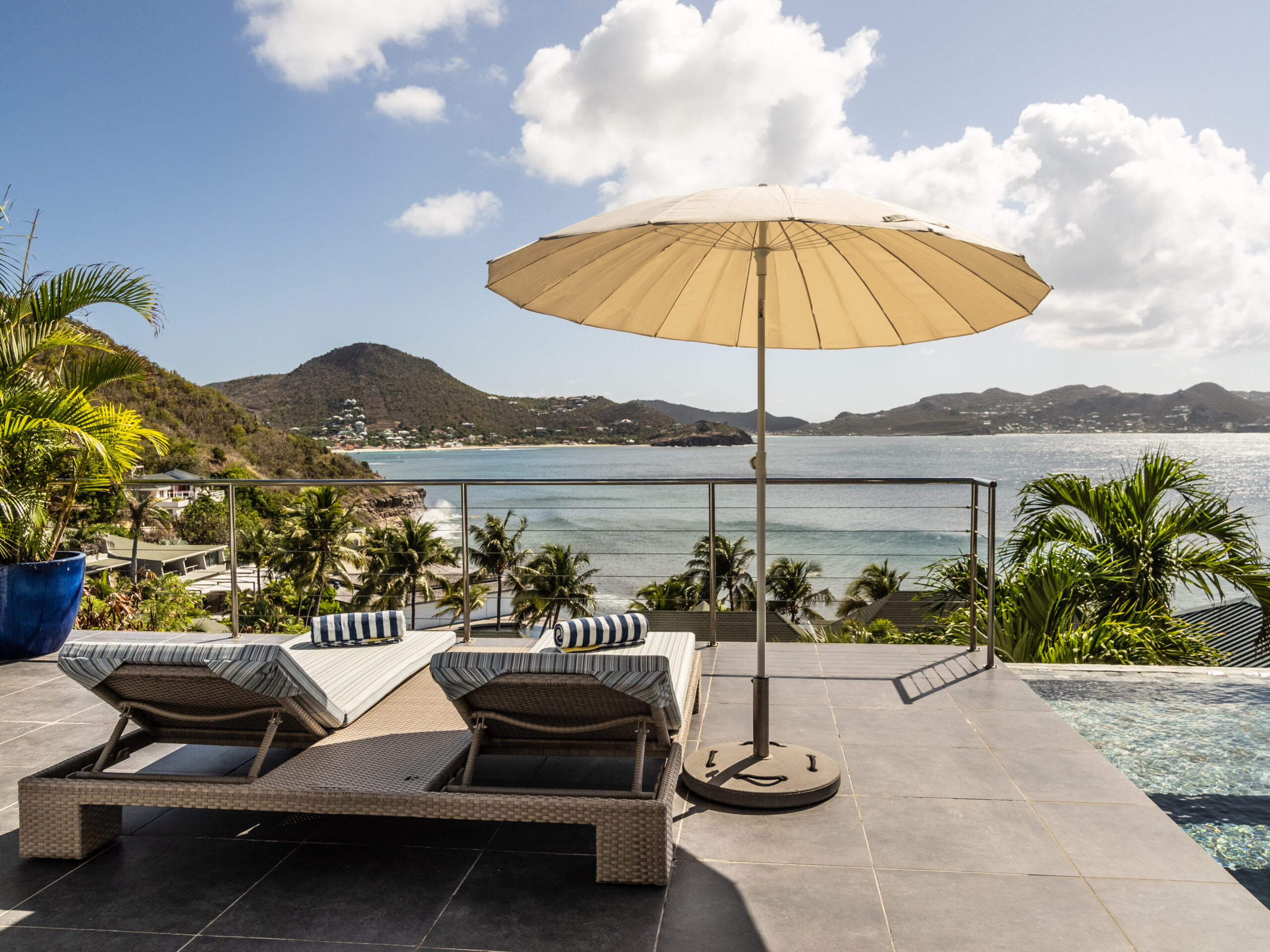 Terrace with sun loungers and umbrella overlooking the Caribbean Sea and hills in a luxury St Barts villa rental.