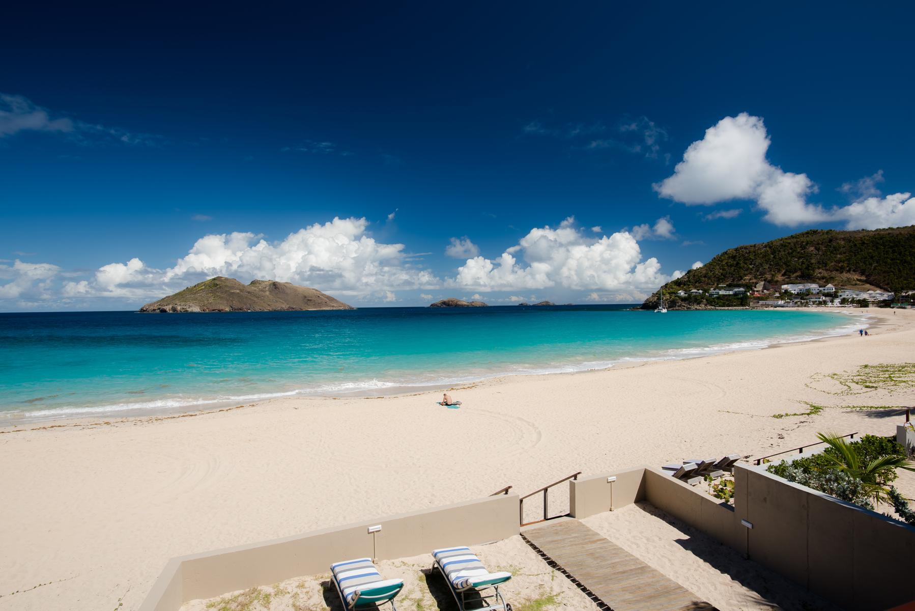 Expansive white sand beach with turquoise waters and clear blue sky, seen from a villa terrace.