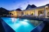 Luxury St Barts villa with illuminated infinity pool at dusk, white loungers, and covered terrace against a mountain backdrop.