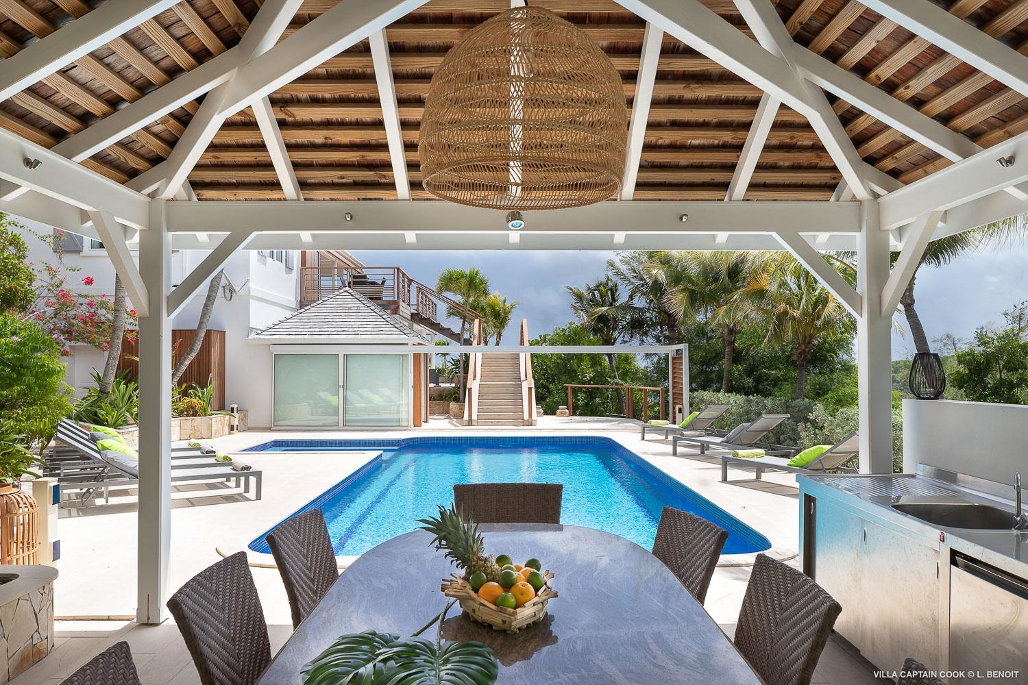 Covered outdoor dining area of a St Barts villa facing a private swimming pool and tropical garden