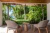 Covered patio at a St Barts villa with woven chairs overlooking lush tropical gardens and palm trees