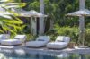 Sunlit poolside at a St Barts villa with white cushioned loungers, umbrellas, and lush tropical gardens.