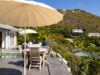 Outdoor dining table with umbrella on a St Barts villa terrace, overlooking lush tropical gardens and hillside views.