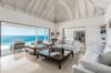 Bright living room in a St Barts villa with white sofas, high ceilings, and panoramic ocean views through sliding doors.