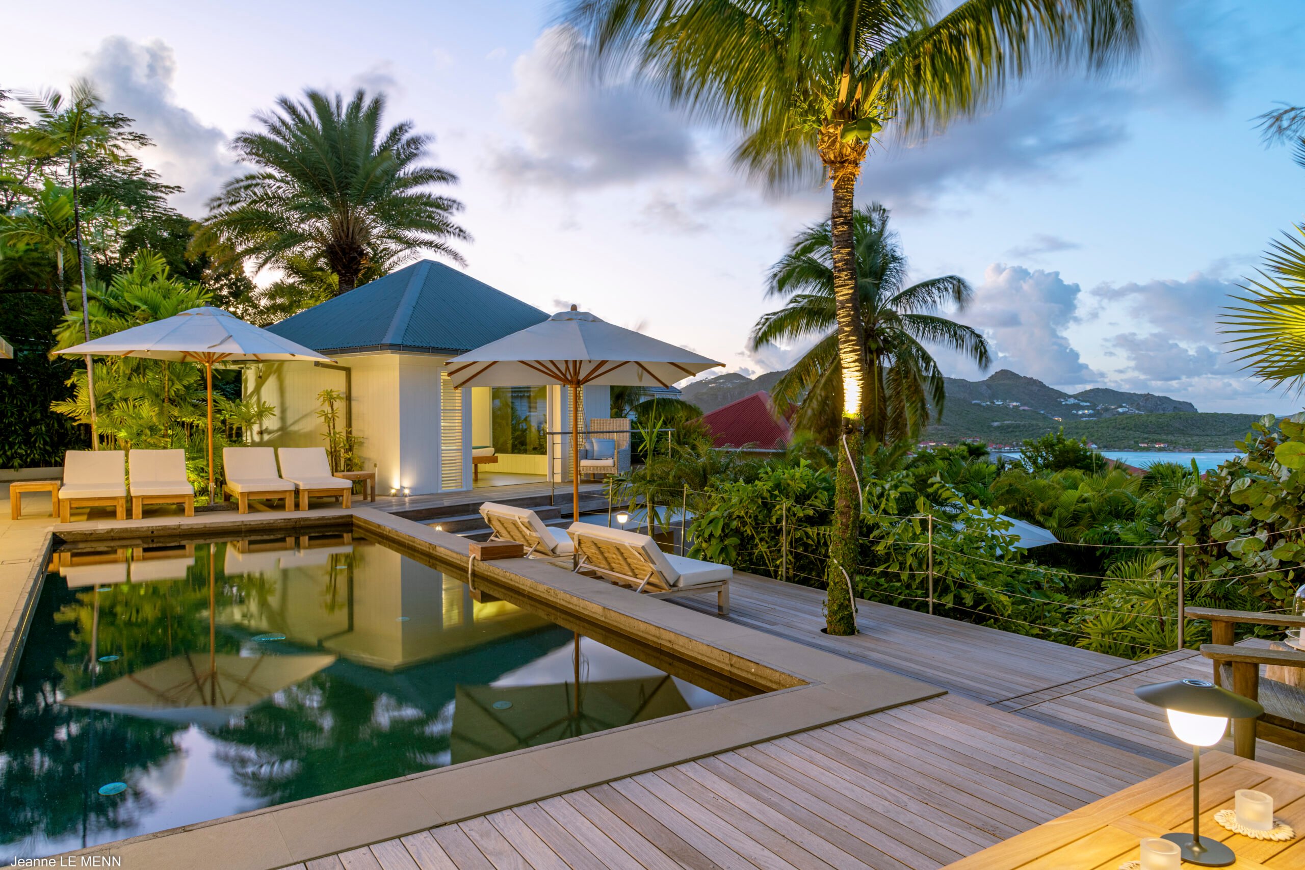Luxury villa pool deck with sun loungers, palm trees, and ocean views at sunset in St Barts vacation rental.