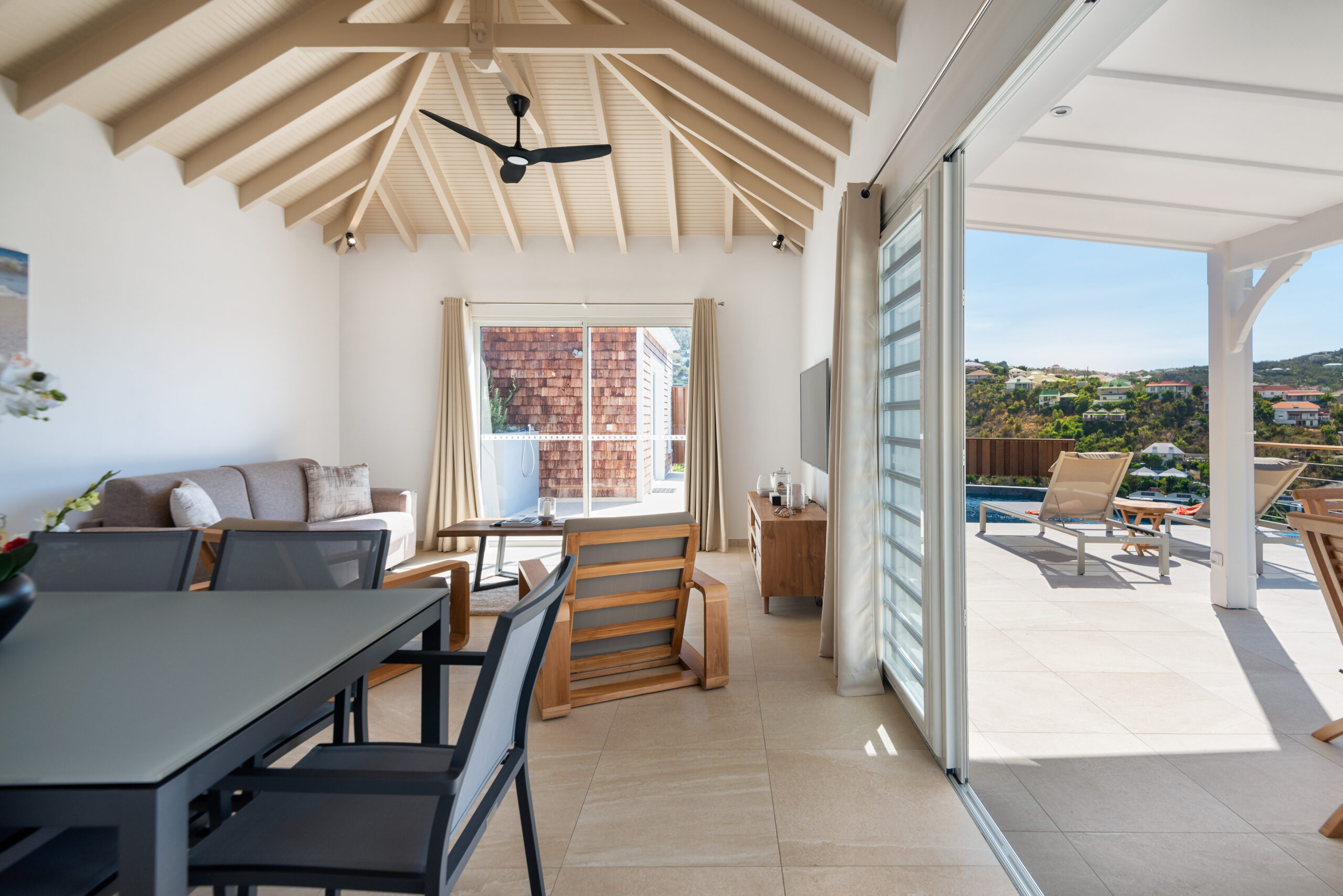Villa lounge and dining area with vaulted ceiling opening to sunny terrace and pool in St Barts luxury rental.