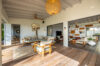 Spacious open living area at Villa Jocapana with natural wood furniture, soft neutral seating, artistic palm tree wall décor, and seamless flow to the indoor lounge and library.