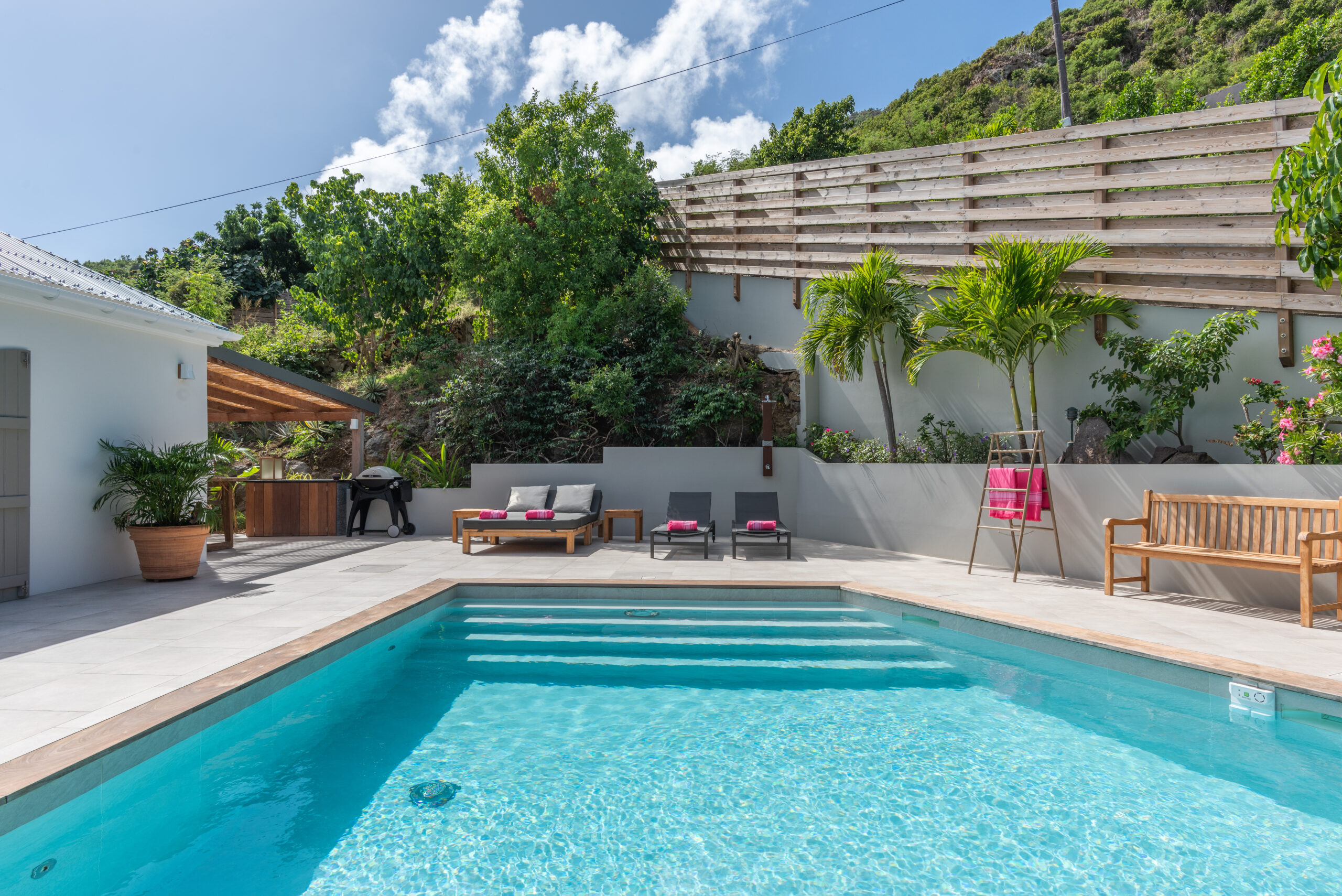 Inviting pool with sun loungers, tropical plants, and hillside backdrop in a St Barts vacation rental villa.