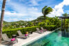 a wooden pool deck with four lounge chairs with pink towels, a private infinity pool, and a panoramic view of the ocean and the hillside