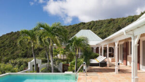 Sunny villa terrace with pool, palm trees, and hillside view in Gouverneur, St. Barts.