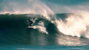 Surfer riding a large wave with water spray in the ocean.