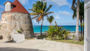 Oceanview villa in St. Jean with historic stone tower and palm trees by the turquoise sea.