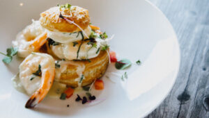 Gourmet shrimp dish with puff pastry and creamy sauce, garnished with herbs and diced vegetables.