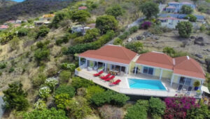 Aerial view of a yellow villa with pool and red roof on a hillside.