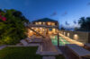 Evening view of luxury St Barts villa with glowing pool, wooden deck loungers, and tropical garden backdrop