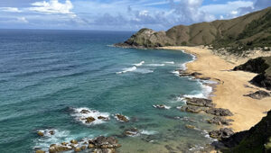 Golden sandy beach in St. Barth with turquoise waves and rugged cliffs along the shore.