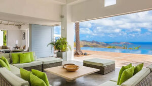 Open-air villa lounge with green cushions, ocean-view infinity pool, and tropical scenery.