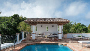 Poolside patio with lounge chairs and shaded seating area, surrounded by greenery.