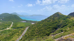 Scenic coastal view of St. Barth with winding roads, green hills, and turquoise sea.