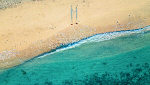 Aerial view of two people standing on a sandy beach near the ocean in St. Barts.