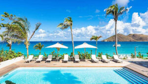 Poolside lounge chairs and umbrellas with ocean and hills in the background in Flamands