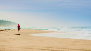 Person walking alone on a wide sandy beach with ocean waves and misty horizon.