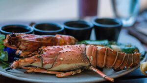 Grilled lobster tail on a plate with dipping sauces in small black bowls.