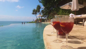 Three glasses of sangria by a curved infinity pool with ocean view