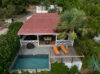 Aerial view of a private villa in St Barts with red roof, tropical palm trees, ocean-view terrace, infinity-style pool, and sun loungers
